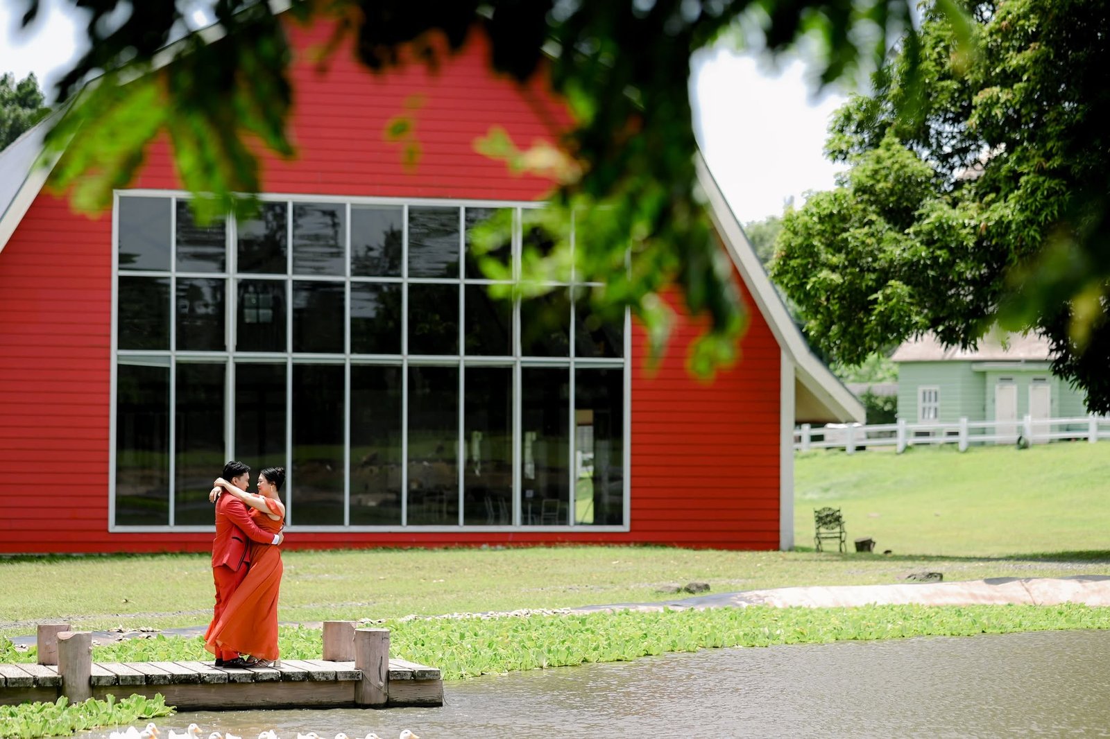 Chie and Cath in an embrace on a jetty, with a red barn behind them.