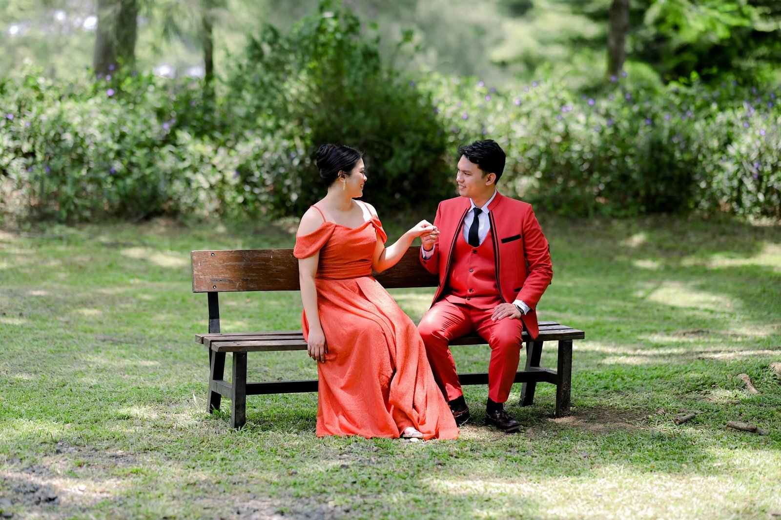 Chie and Cath sitting together on a wooden bench, hand in hand.